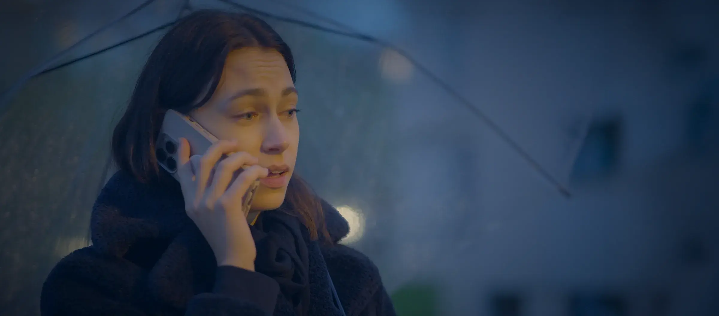 A woman under an umbrella on a phone call at night