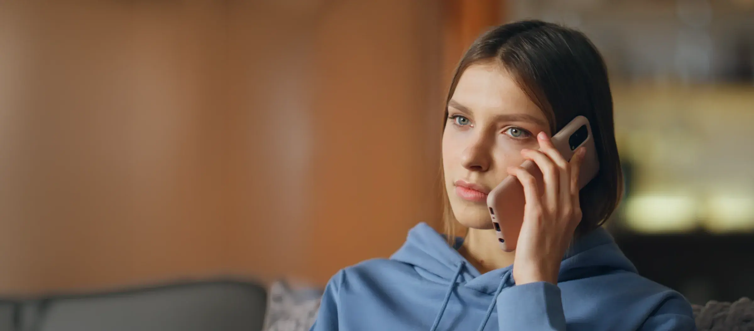 A woman in a blue hoodie on a phone call in her living room