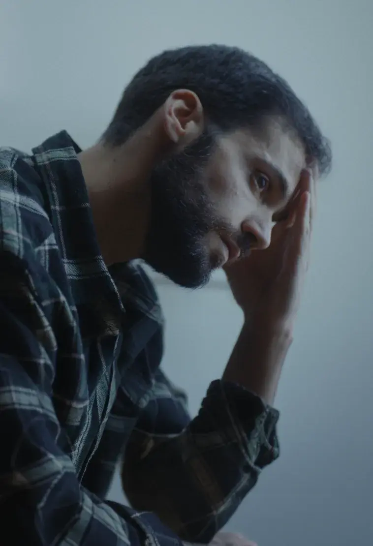 A man in a plaid shirt holding his head, thinking