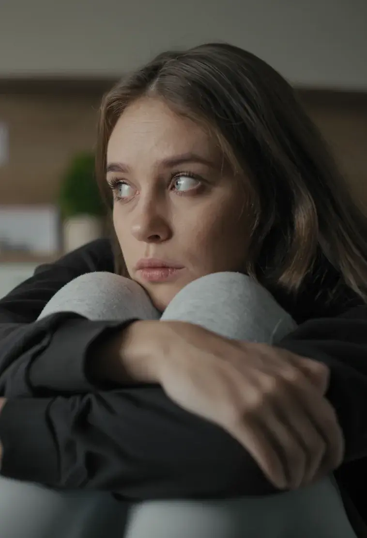 A young woman hugging her knees, looking away