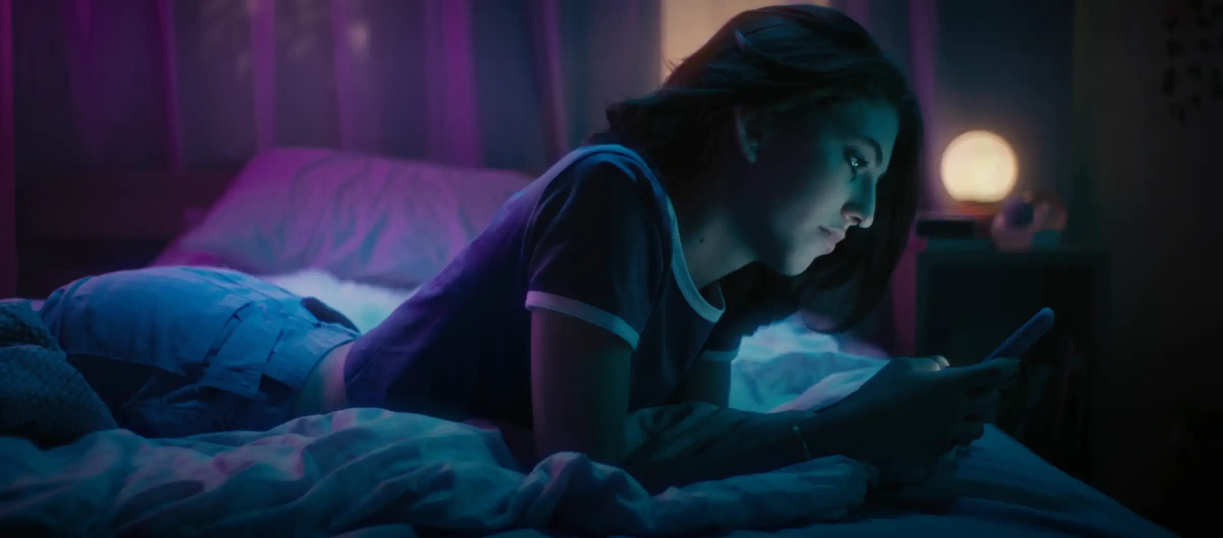 A teen on a bed at night looking at a phone